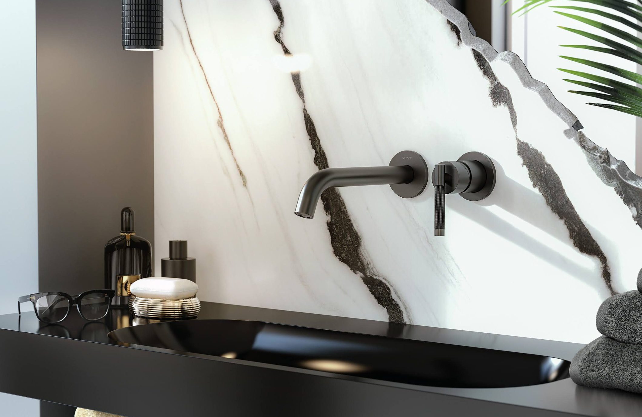 A modern bathroom features a sleek black sink with a wall-mounted faucet and handle. The wall behind the sink has a striking white and gray marble design. The countertop holds a soap dispenser, small towels, and glasses. A plant adds a touch of greenery.